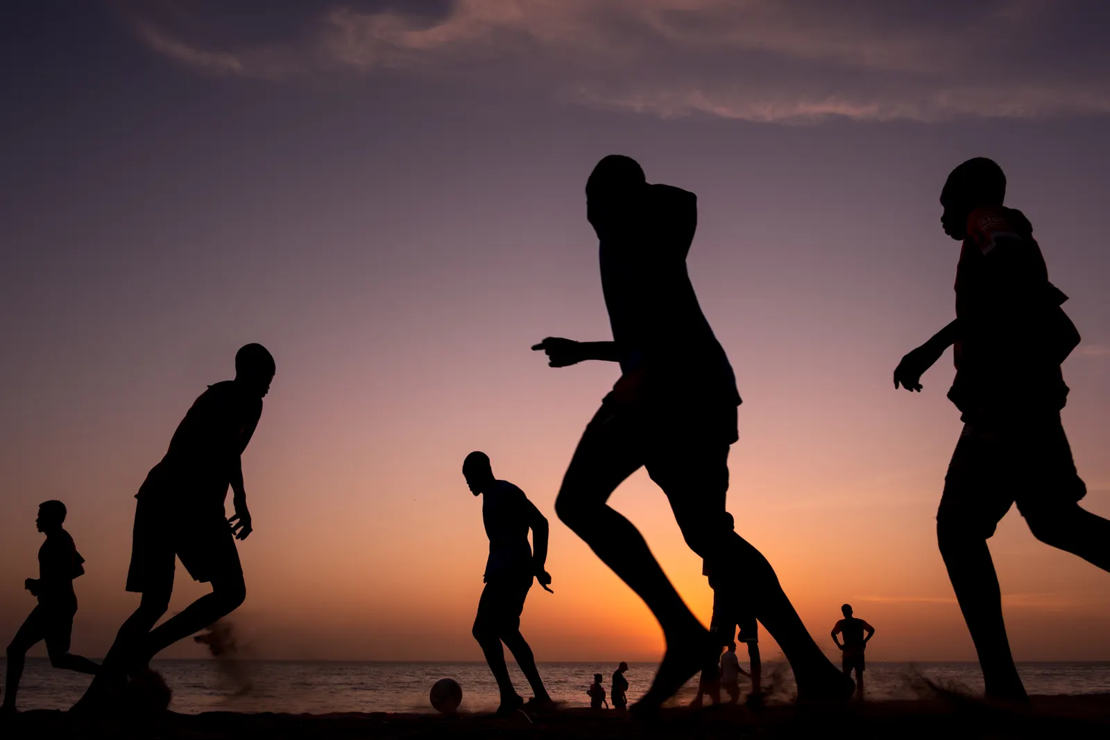 夕暮れの浜辺でボールを追うビーチサッカーのシルエット